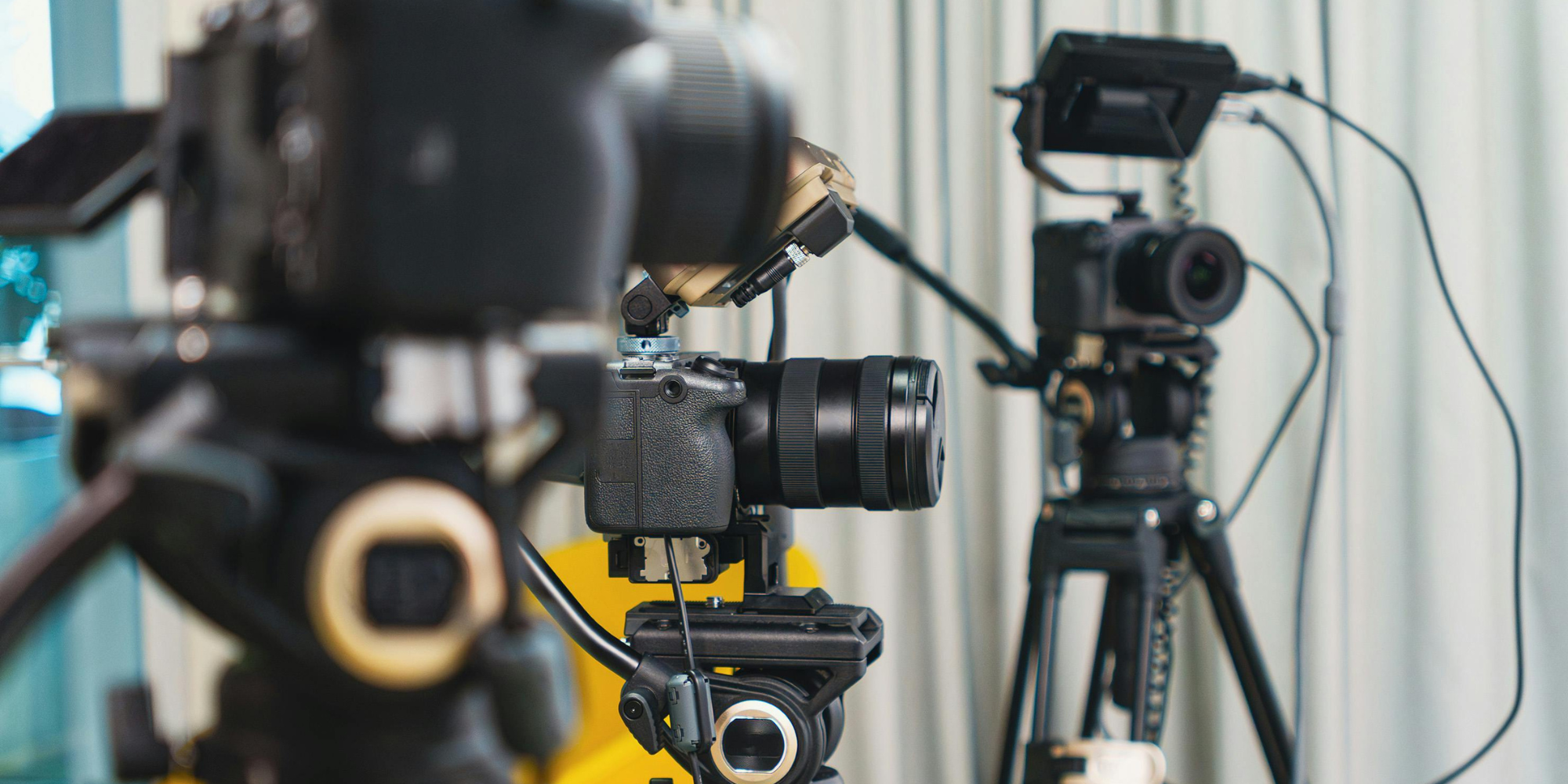 setup-camera-multicamera-social Primo piano di una videocamera mirrorless montata su uno stabilizzatore professionale a tre assi (gimbal) con uno schermo di monitoraggio visibile sullo sfondo e un'altra camera su cavalletto, pronte per una ripresa multicamera.